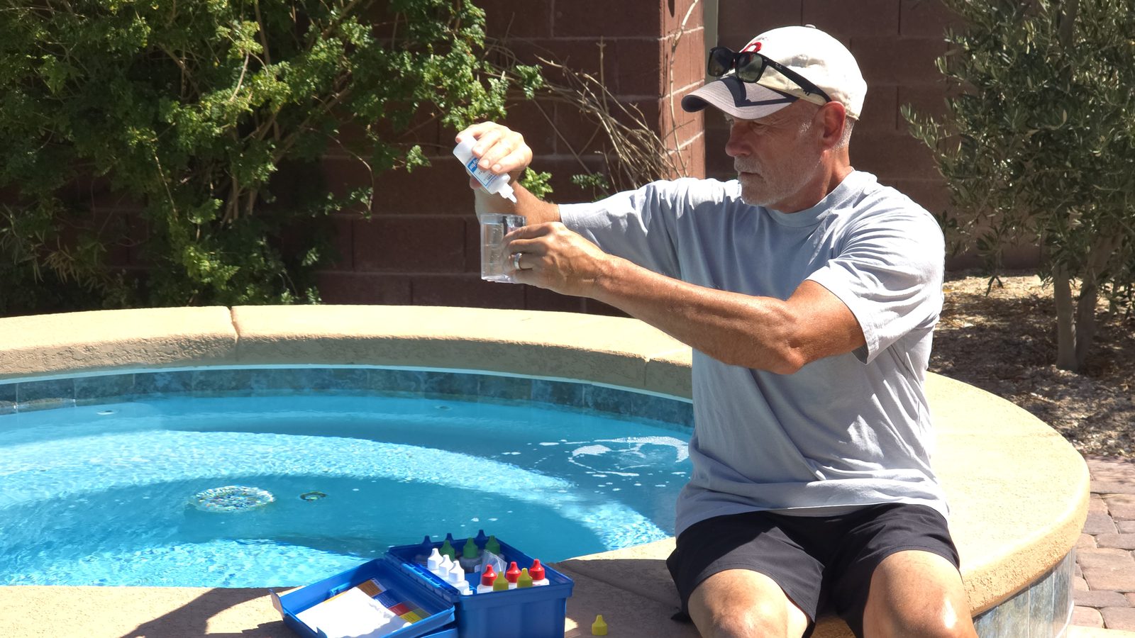 Michael Brown of AquaVision Pool Care sitting on a spa edge in a Las Vegas Valley backyard, running a water chemistry test beside a clear blue pool