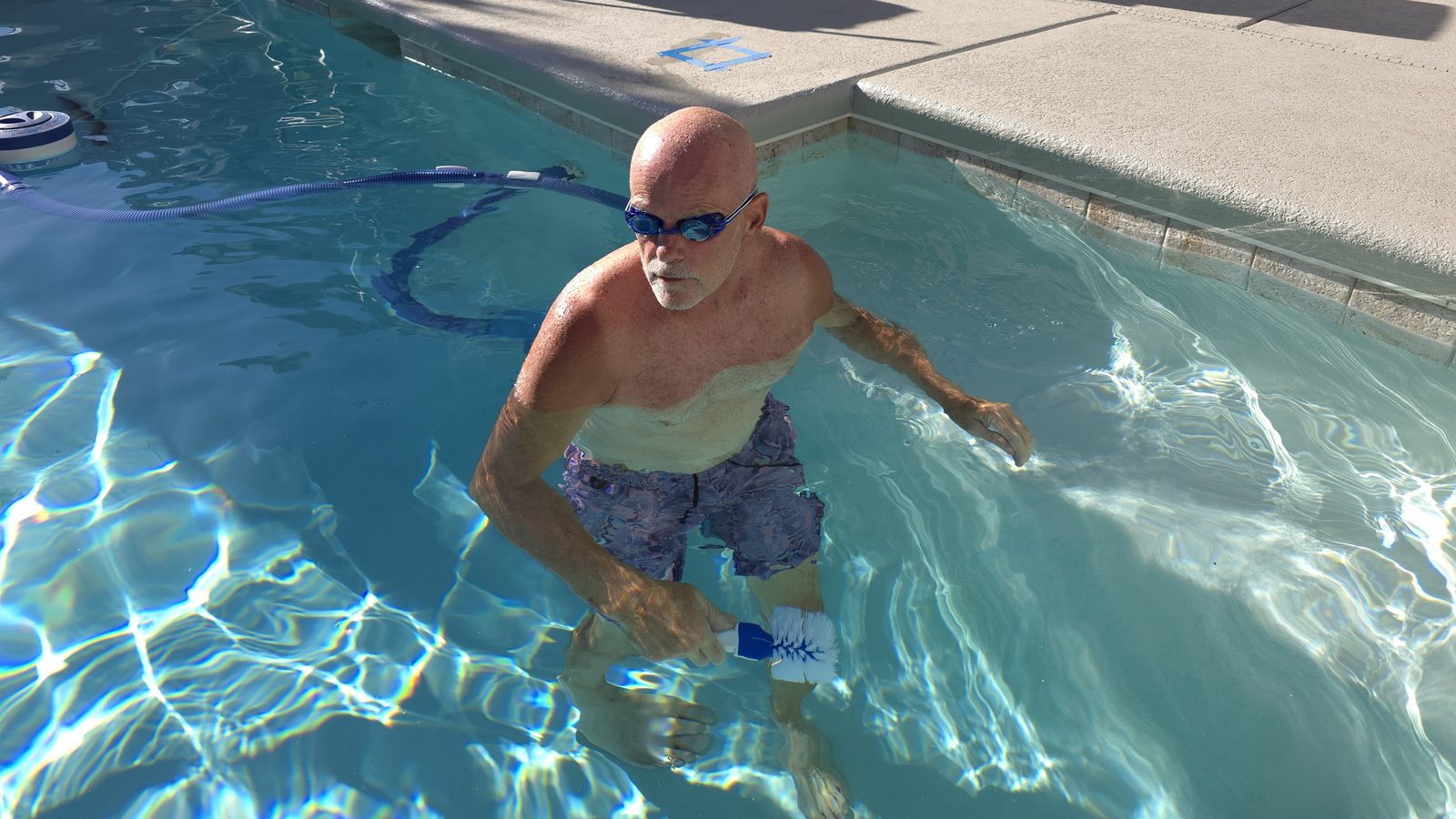 Michael Brown of AquaVision Pool Care standing in a clear Las Vegas Valley residential pool holding a scrub brush, goggles on, mid-service