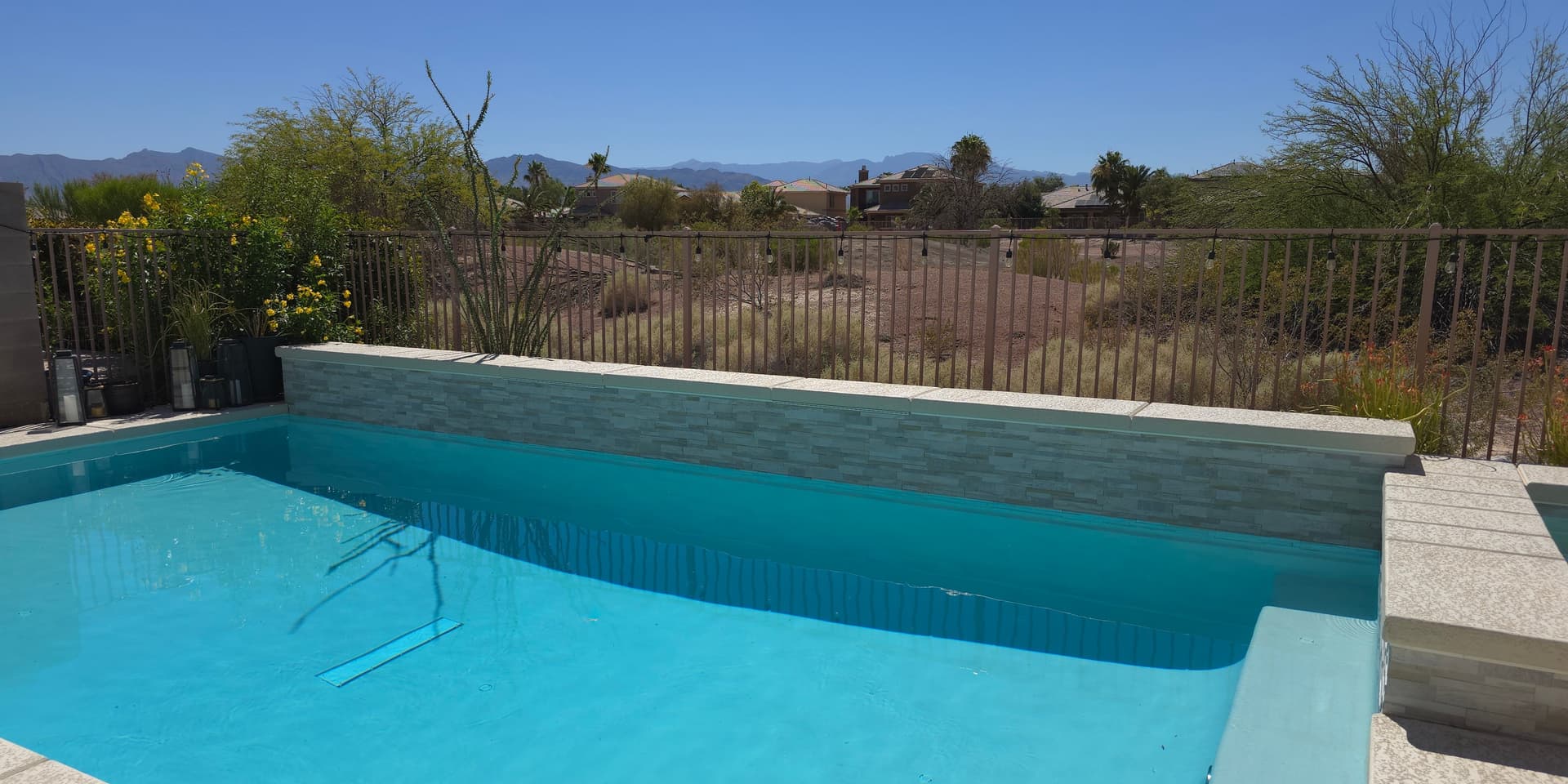 Clear residential pool with tiled spa wall, desert vegetation, iron fence, and Spring Mountains backdrop in Enterprise, Las Vegas