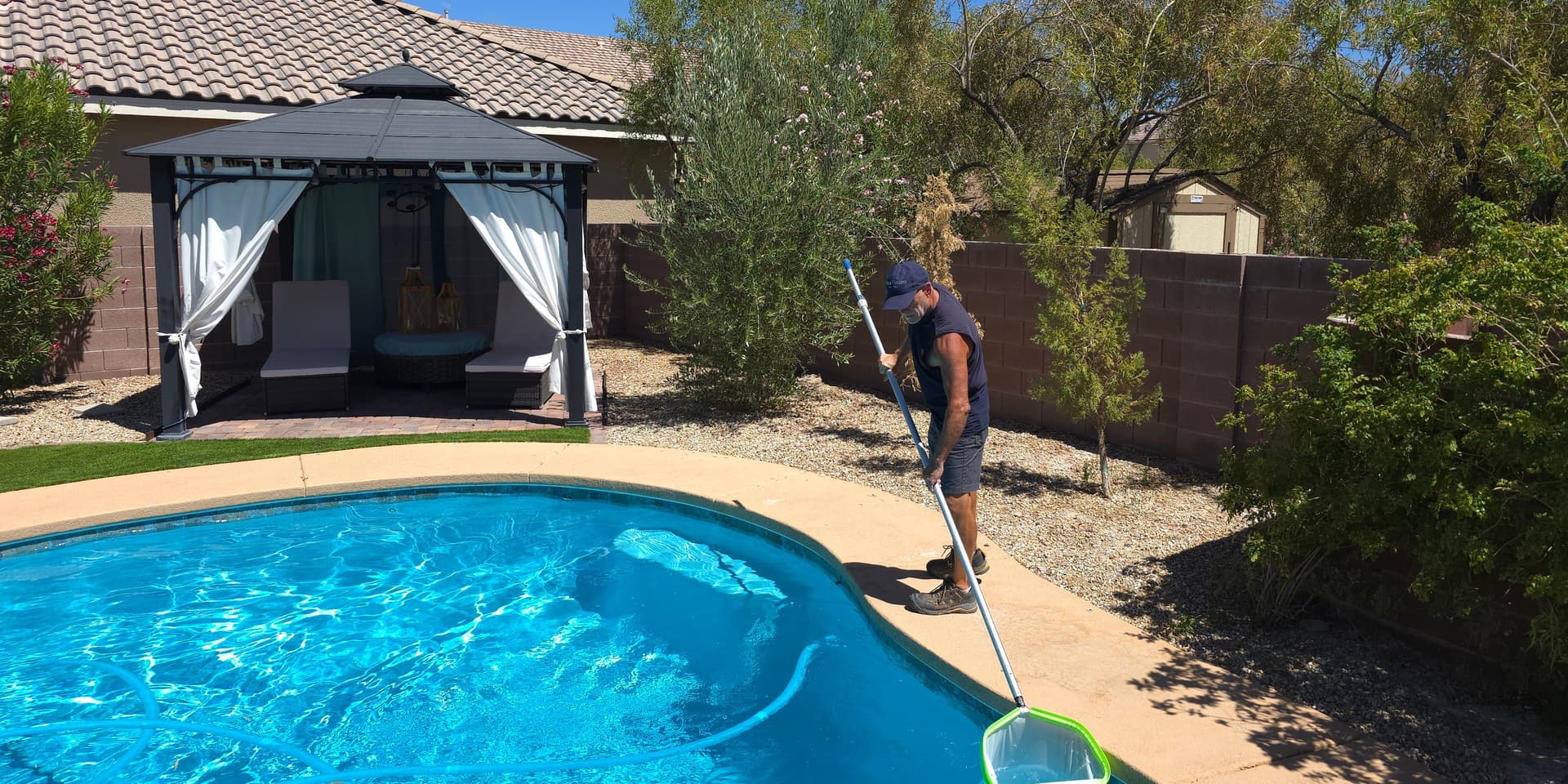 Michael Brown, AquaVision Pool Care Certified Pool Operator, skimming a residential pool with a backyard gazebo in Summerlin, Las Vegas