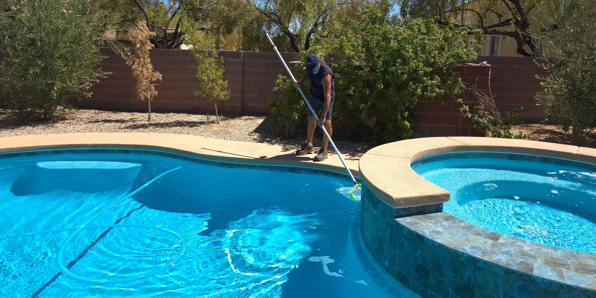 AquaVision Pool Care Certified Pool Operator skimming a residential pool and spa with a Las Vegas Valley desert backdrop